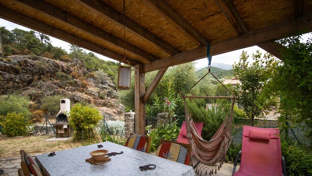 Un espace extérieur abrité, aménagé pour les repas, avec une table, des chaises et un hamac.