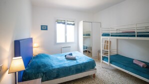 Une chambre avec un lit simple, un lit superposé, une fenêtre avec des rideaux, un radiateur et une lampe.