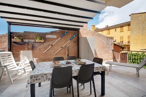 Une terrasse avec une table dressée pour le repas, entourée de chaises, et un mur de briques orné de plantes et de cannes à pêche.