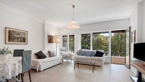 Amplia sala de estar con un sofá blanco, una mesa de comedor con mantel azul y un ventanal con vistas a árboles.