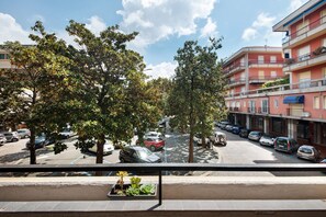 A street view with parked cars, trees, and multi-story buildings.