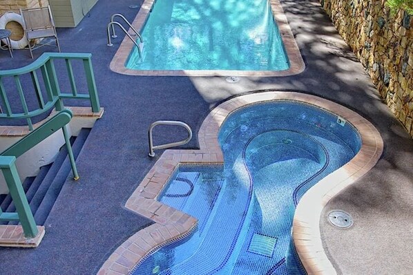 A swimming pool with a wavy edge design, a small hot tub, and a stone wall.