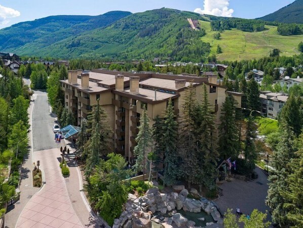 A multi-story hotel with a central courtyard, surrounded by lush greenery and mountains in the background.
