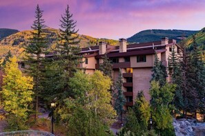 Un edificio a più piani dal design moderno, circondato da alberi e colline.
