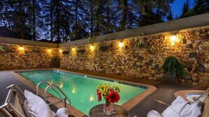 Ein Poolbereich im Freien mit Steinwänden, Liegestühlen und einem Tisch mit Blumen.