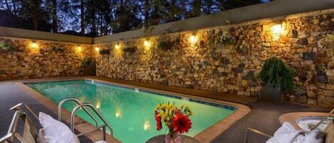 An outdoor pool area with stone walls, lounge chairs, and a table with a vase of flowers.