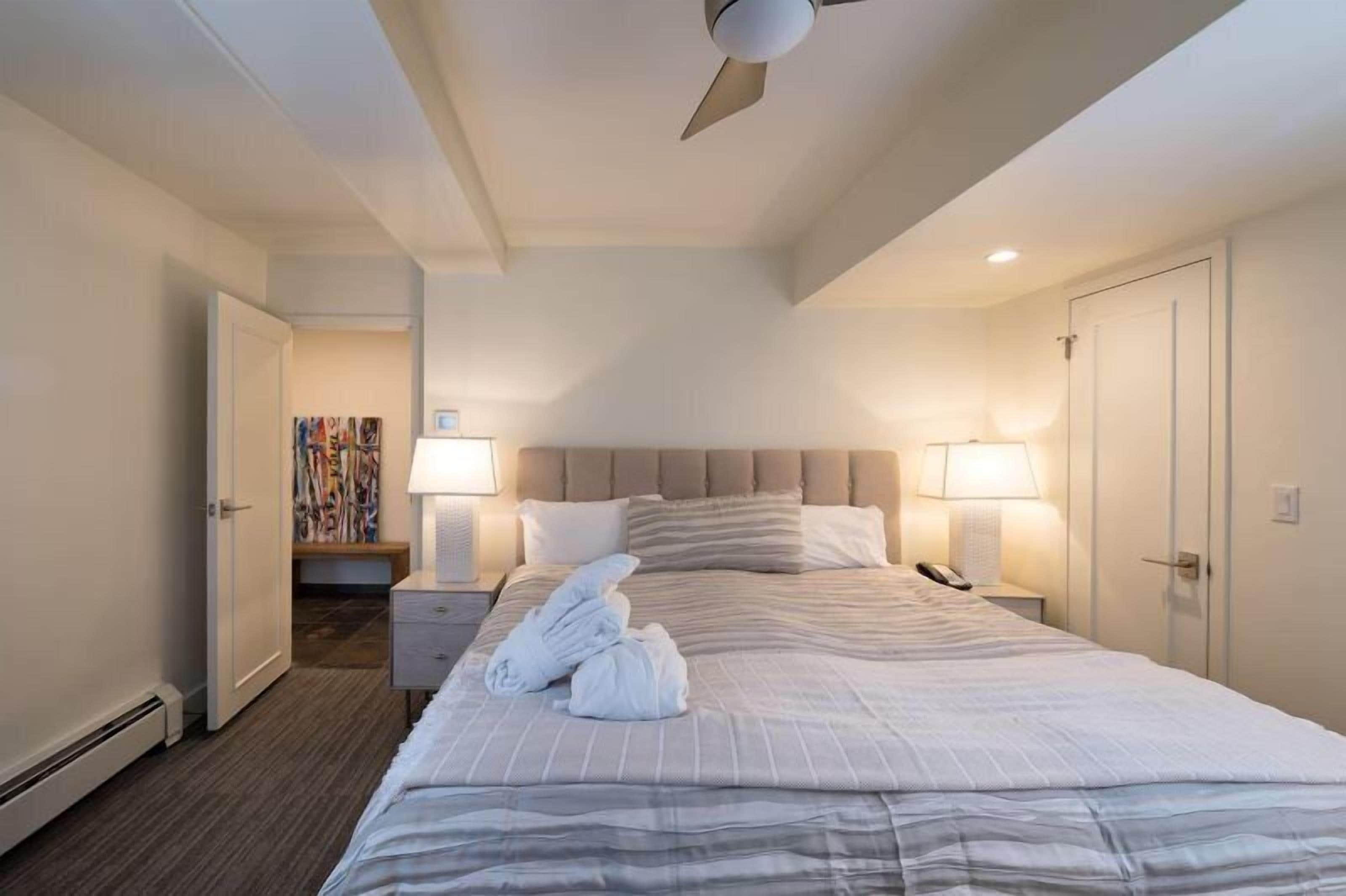 Una habitación de hotel con una cama grande, dos lámparas de noche, un ventilador de techo y un teléfono junto a la cama.