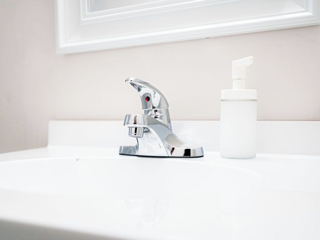 Un lavamanos de baño con grifo cromado y dispensador de jabón blanco.