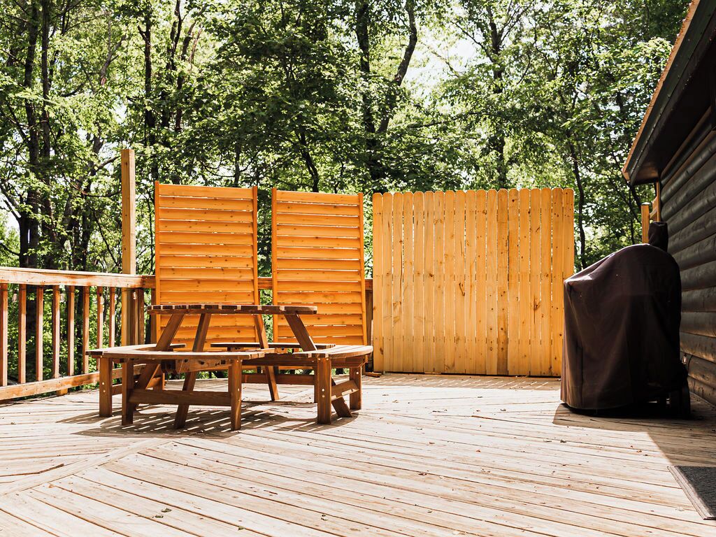 Una terraza de madera con una mesa, sillas, una parrilla cubierta y una cerca de madera.