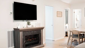 A living room with a fireplace, a mounted TV, and a dining area with chairs. - Soak In the Hot Tub @ County Top Cabin - Near I-77 & the Blue Ridge Parkway (Fancy Gap)