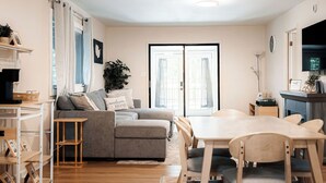 A living room with a sofa, a dining table with chairs, a TV, and a bookshelf. - Soak In the Hot Tub @ County Top Cabin - Near I-77 & the Blue Ridge Parkway (Fancy Gap)