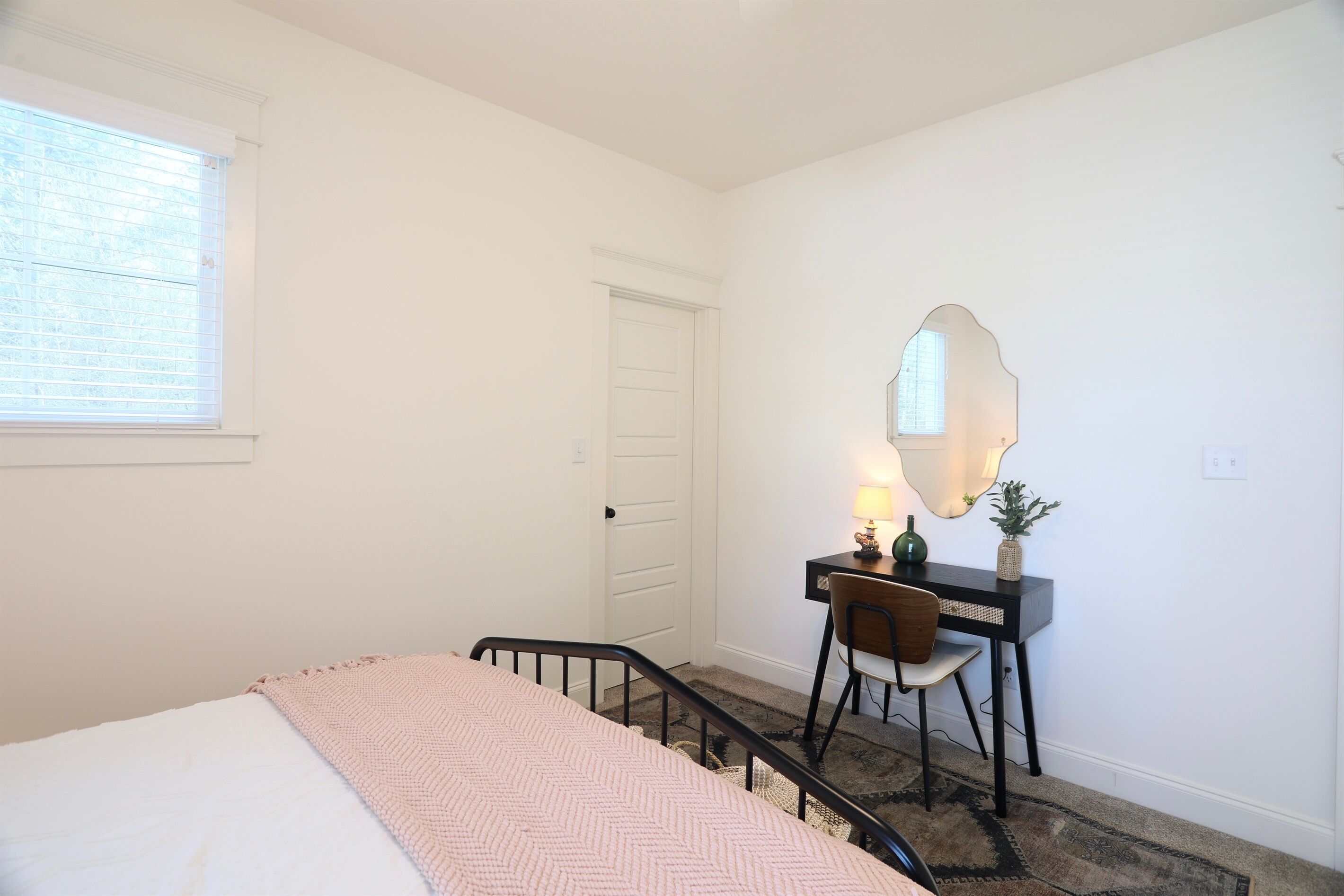Un dormitorio con cama, escritorio, silla, espejo y ventana.