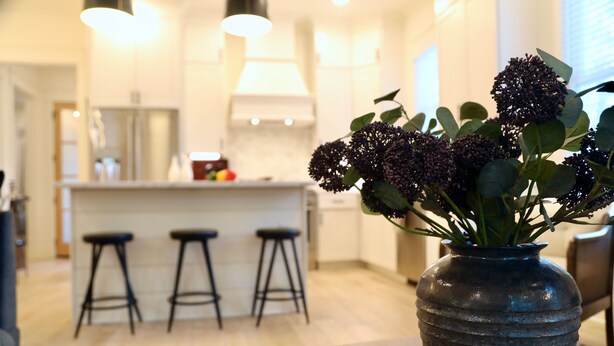 A modern kitchen with a central island, bar stools, and a vase with flowers on a table.