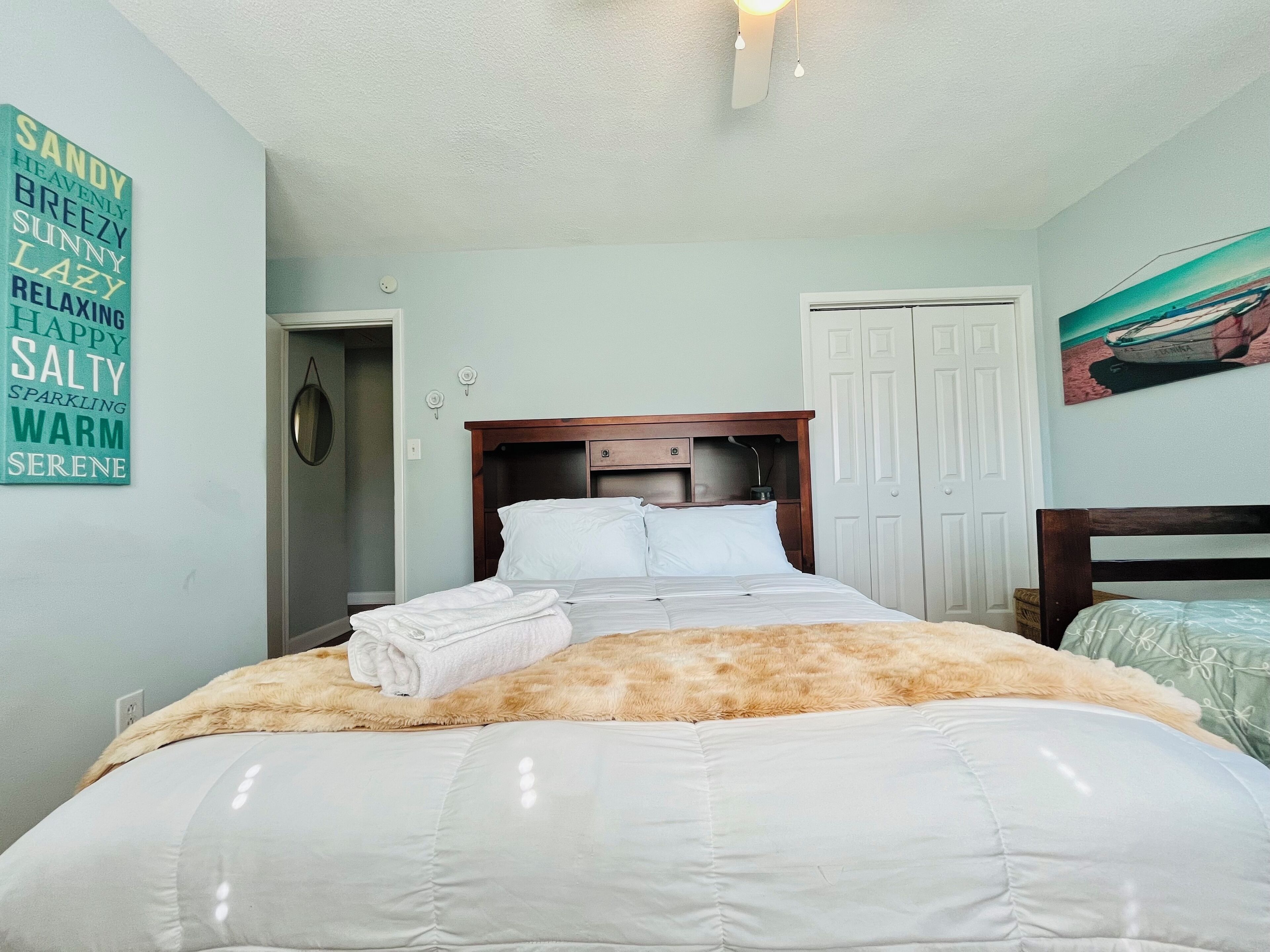 A neatly made bed with a fluffy blanket, a wooden headboard, and a wall with a list of words.