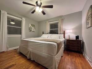 Une chambre à coucher comprenant un lit, une table de chevet, un ventilateur de plafond et une fenêtre avec des stores.