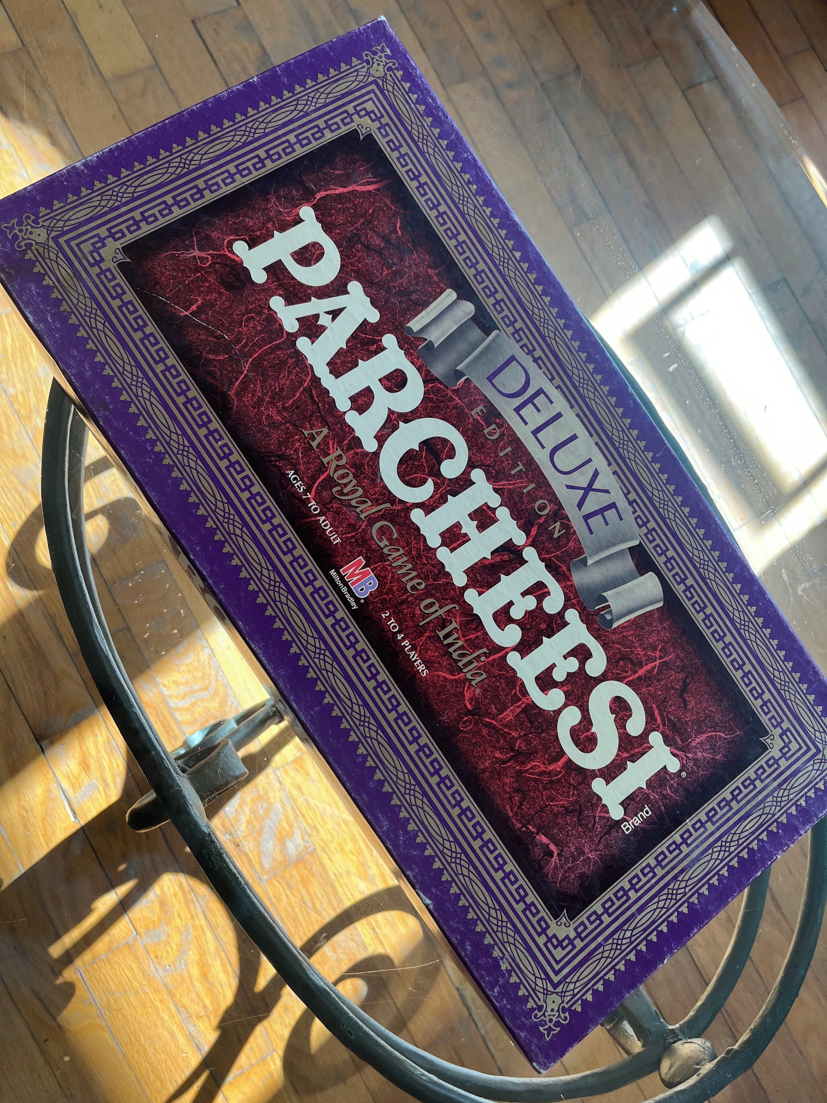 A book titled "PARCHEESI DELUXE" on a glass table.