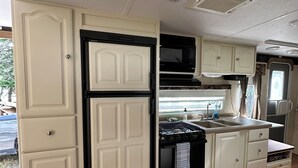 A compact RV kitchen with white cabinetry, a black stove, a microwave, and a sink. - Montana Moon on the Lake "Outback" RV #7 (Babb)