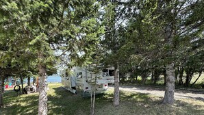 A recreational vehicle (RV) parked in a wooded area with trees surrounding it. - Montana Moon on the Lake "Outback" RV #7 (Babb)