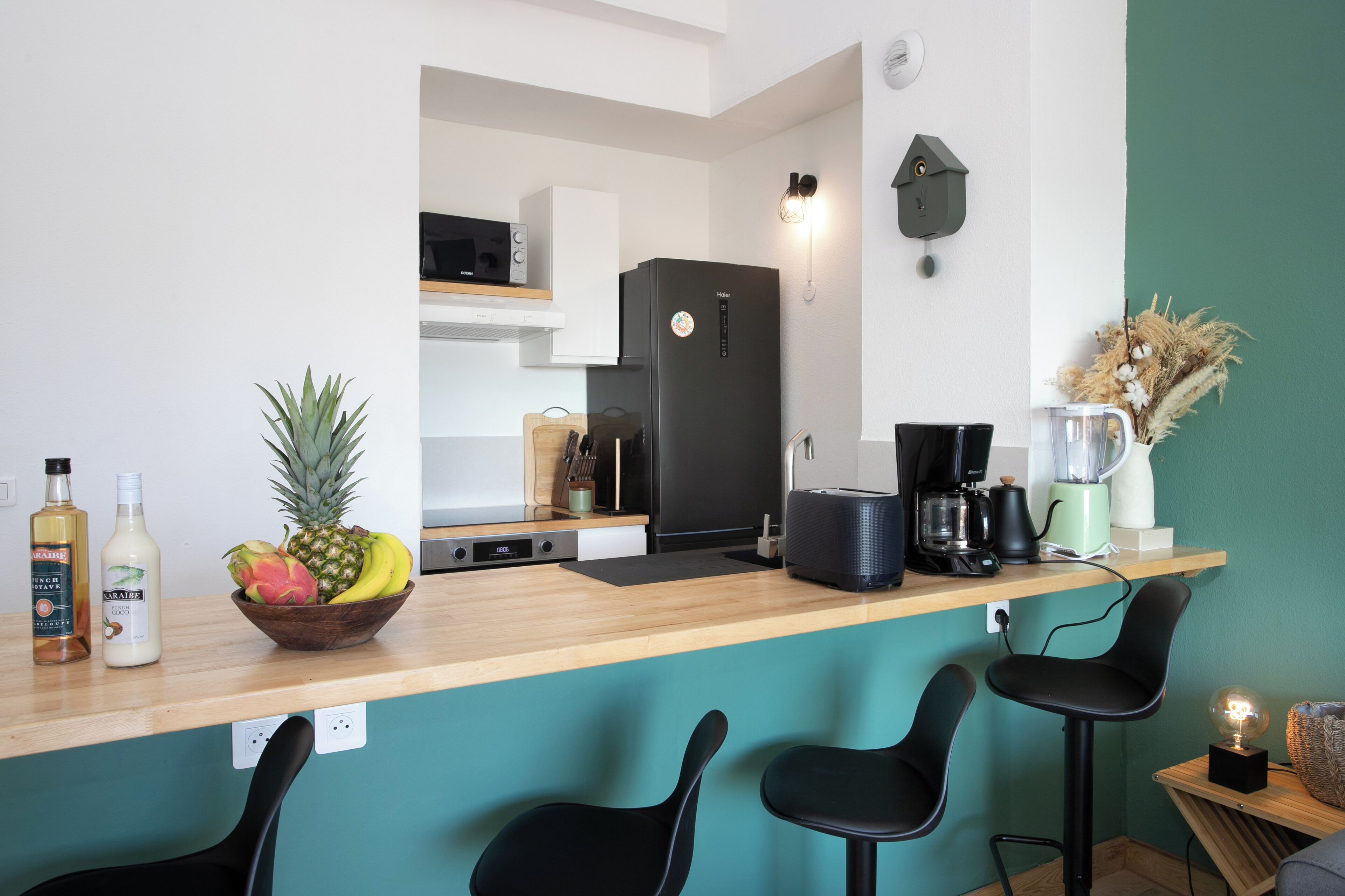 A modern kitchen with a wooden countertop, black chairs, a black refrigerator, and a teal wall.
