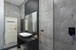 Une salle de bain moderne avec un lavabo blanc, des plans de travail foncés et des murs en marbre gris.