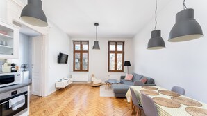 Una cocina moderna con armarios blancos, un microondas y una estufa. Hay un comedor con una mesa y sillas, y un sofá al fondo.