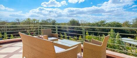 A terrace with wicker furniture and a glass table, overlooking a lush landscape.