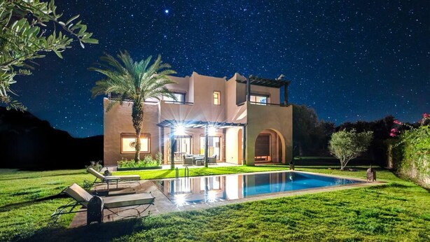 Een modern huis met een zwembad, een terras en een sterrenhemel.