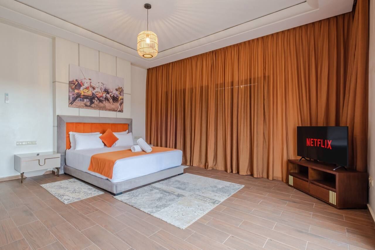 Ein modernes Schlafzimmer mit Bett, Fernseher und einem großen Fenster mit Vorhängen.