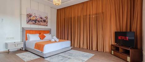 A modern bedroom with a bed, a TV, and a large window with curtains.