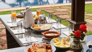 Een buiten eethoek met een tafel gedekt voor het ontbijt, inclusief borden met eten, glazen sinaasappelsap en een waterkan.