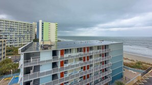 Ein mehrstöckiges Hotel mit Balkonen mit Blick auf einen Strand, einem Parkplatz und den Ozean.