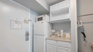 Eine kompakte Küche mit weißen Schränken, einem Kühlschrank, einer Mikrowelle, einer Kaffeemaschine und einem Telefon.