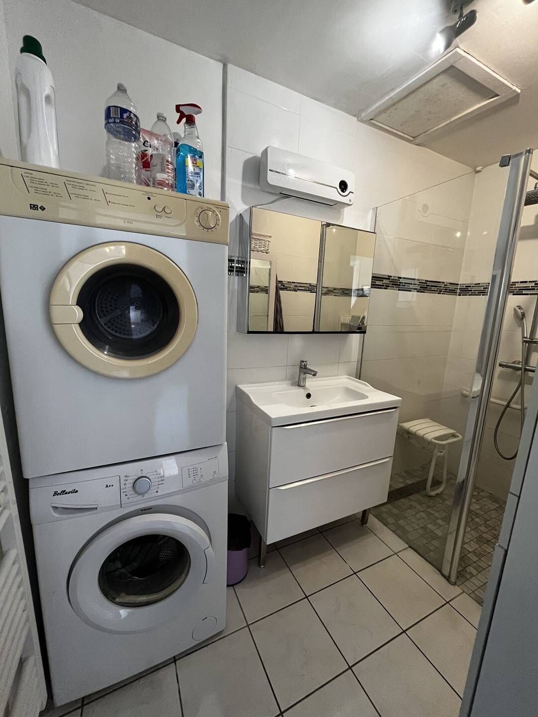 A compact bathroom with a washing machine, a sink, and a shower.