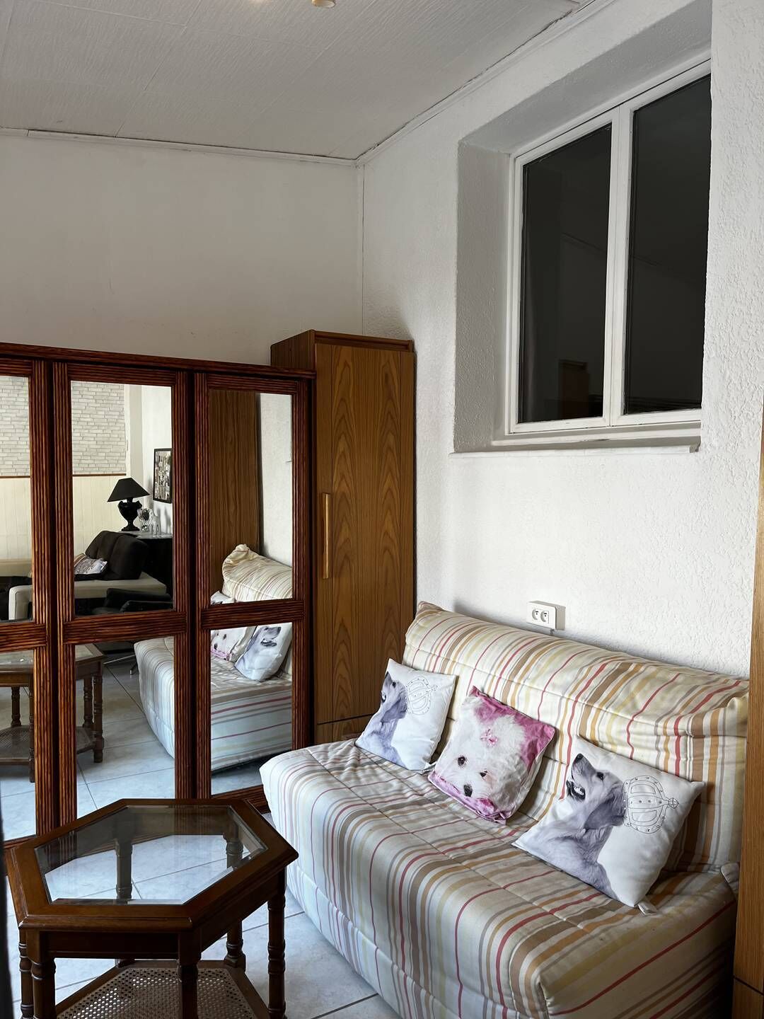 A cozy living room with a striped sofa, a wooden cabinet, and a glass-top coffee table.