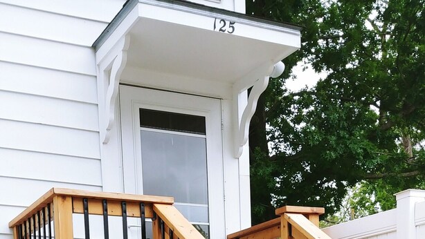 Una escalera de madera con barandilla que conduce a una casa blanca con el número 125 en la fachada.