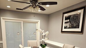 A dining area with a table set for four, a ceiling fan, and a framed picture on the wall.