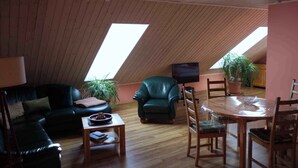 A cozy loft-style living space with a sloped ceiling, a dark green leather sofa, a wooden dining table with chairs, and a television. - Ferienwohnung mit Fahrrädern und Garten (Müncheberg)