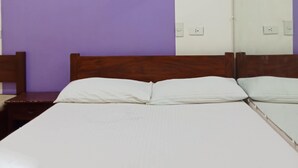 A room with a bed, a wooden headboard, a wall with a painting, and a white wall with a mirror. - Moonlight lodge (Puerto Princesa)