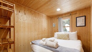 Une pièce en bois avec un lit, une échelle en bois, une fenêtre et un tableau encadré accroché au mur.