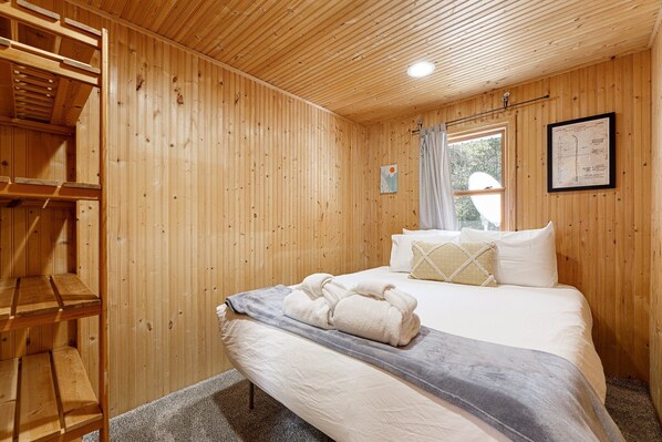 Une pièce en bois avec un lit, une échelle en bois, une fenêtre et un tableau encadré accroché au mur.