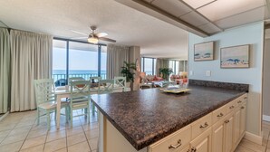 A spacious kitchen with a granite countertop, light-colored cabinetry, and a view of the ocean through large windows.
