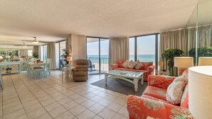 A spacious living area with a large window overlooking the sea, a dining area with a table and chairs, and a seating area with a sofa and armchairs.