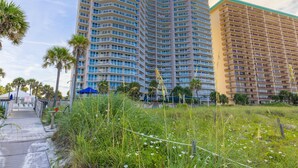 Un hotel moderno de altura con múltiples balcones, un paseo marítimo y vegetación circundante.