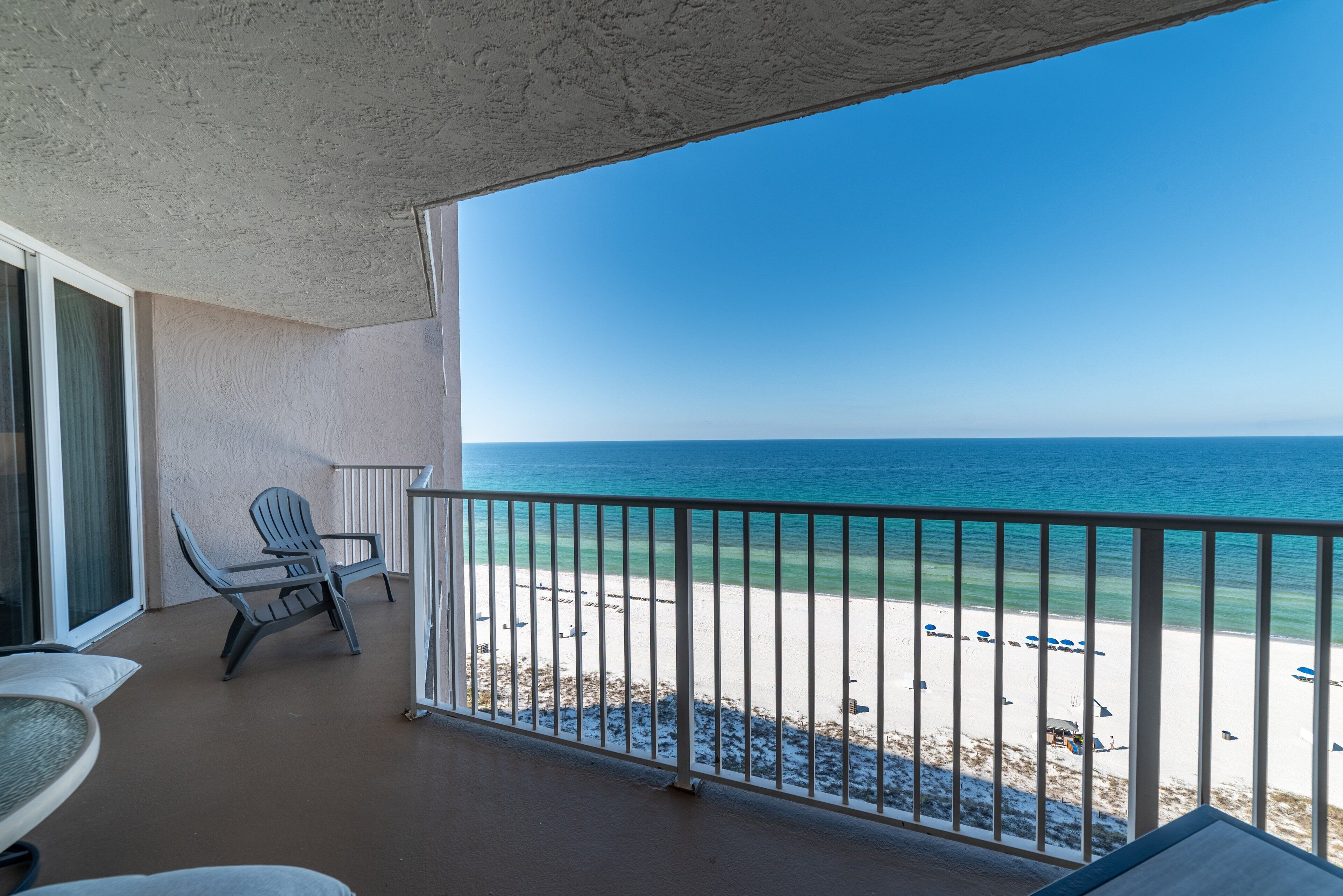 Ein Balkon mit Blick auf den Strand, ein Stuhl und ein Tisch.