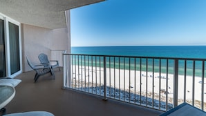 Un balcón con vista a la playa, una silla y una mesa.