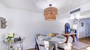 Un espace repas comprenant une table ronde, des chaises, un luminaire suspendu et un chariot en verre contenant divers objets.
