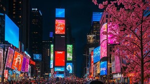 Una calle urbana concurrida de noche, con vallas publicitarias iluminadas y una multitud de personas.