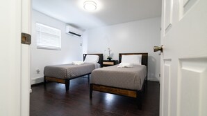 Un dormitorio con dos camas individuales, una mesita de noche, un equipo de aire acondicionado y una ventana con persianas.