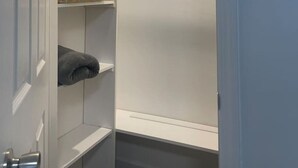 Un armario con estantes blancos, una barra para colgar ropa y una toalla enrollada.