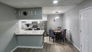 Een moderne keuken met een centraal eiland, een eethoek met tafel en stoelen, en een gang naar een deur.